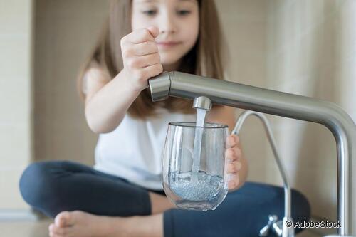 Ein Kind füllt ein Glas am Wasserhahn.