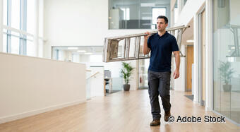 Facility Management: Person mit einer Leiter in einem Bürogebäude.