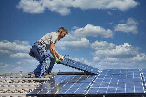 Ein Arbeiter montiert eine PV-Anlage auf einem Dach. Ein Arbeiter montiert eine PV-Anlage auf einem Dach.