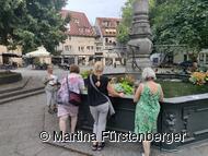 Das Bild zeigt den Brunnen auf dem Hafenmarkt. Um diesen stehen Personen und bei Ihnen steht eine Stadtführerin. Das Bild zeigt den Brunnen auf dem Hafenmarkt. Um diesen stehen Personen und bei Ihnen steht eine Stadtführerin.