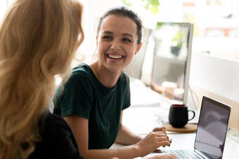 Zwei Frauen sitzen an einem Schreibtisch und schauen sich etwas am Laptop an