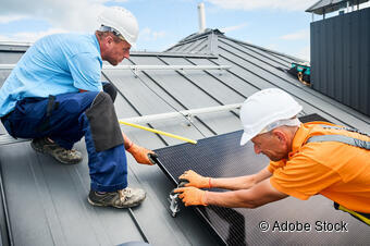 Zwei Männder mit Bauhelmen montieren eine Solaranlage auf einem dach. Zwei Männder mit Bauhelmen montieren eine Solaranlage auf einem dach.